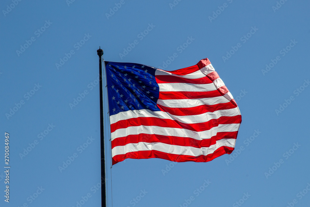 Fototapeta premium USA American flag waving in the wind on clear blue sky in background