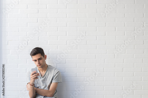 young man with mobile phone on white brick background