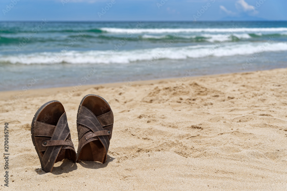 Beach vacation scene of sandal shoes in a sand against sea and blue sky Beach vacation scene of sandal shoes in a sand against sea and blue sky