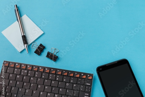 Workspace with wireless keyboard, smartphone, pen and stickers on cyan background. View from above