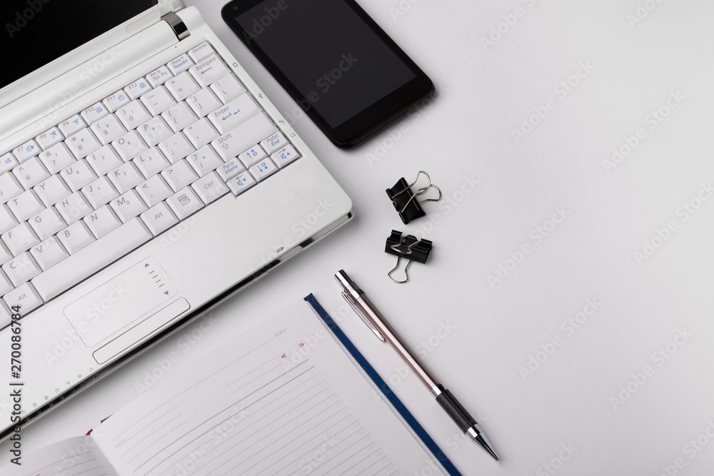 Workspace with laptop, smartphone, pen and datebook on white background. View from above Workspace with laptop, smartphone, pen and datebook on white background. View from above