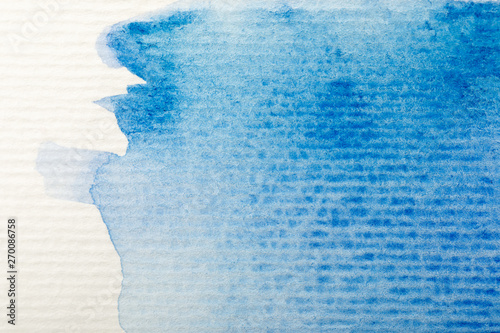 close up view of blue watercolor paint spill on white textured paper background