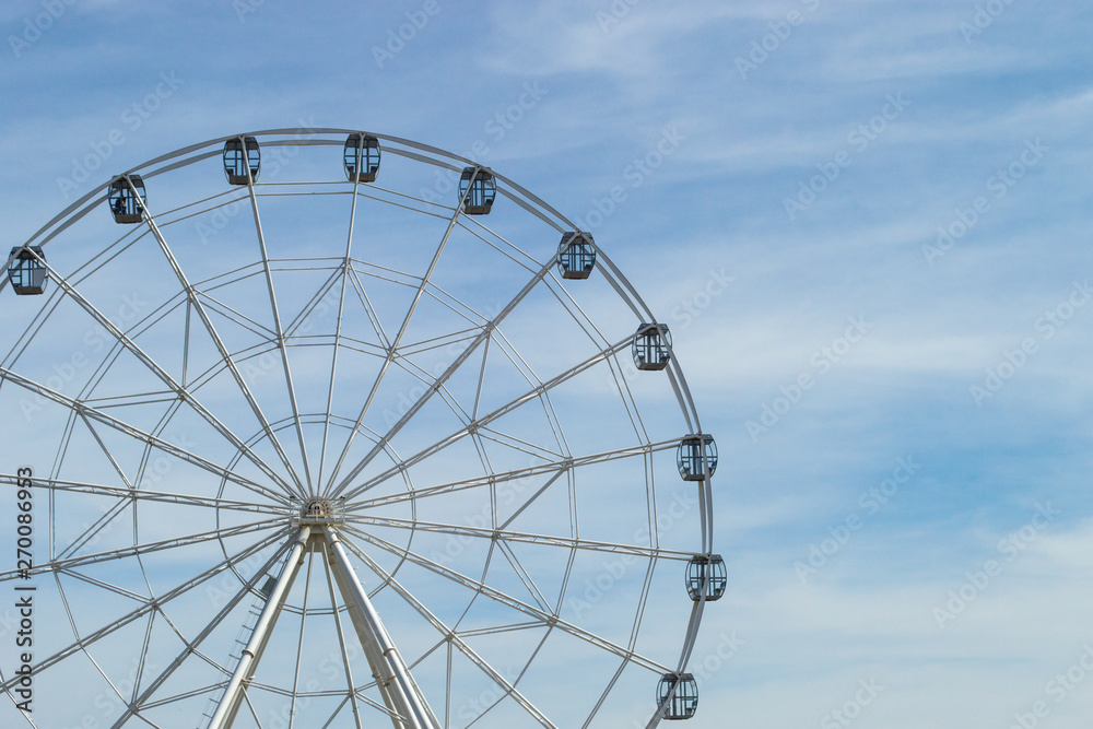 White Ferris wheel with glass light-blue cabins against the blue sky. Wheel in amusement park. Front view, copy space. White Ferris wheel with glass light-blue cabins against the blue sky. Wheel in amusement park. Front view, copy space.