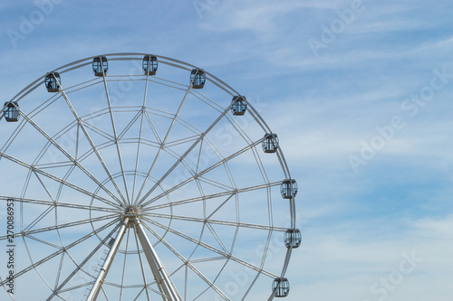 White Ferris wheel with glass light-blue cabins against the blue sky. Wheel in amusement park. Front view, copy space.