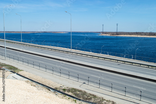 Panorama of big river and riverside with roadway. Empty asphalt highway and blue river nature landscape, sunny day.