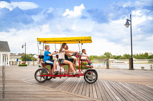 Young happy family riding a double surrey tandem bicycle on a large ocean boardwalk. Outdoor summer fun with kids photo
