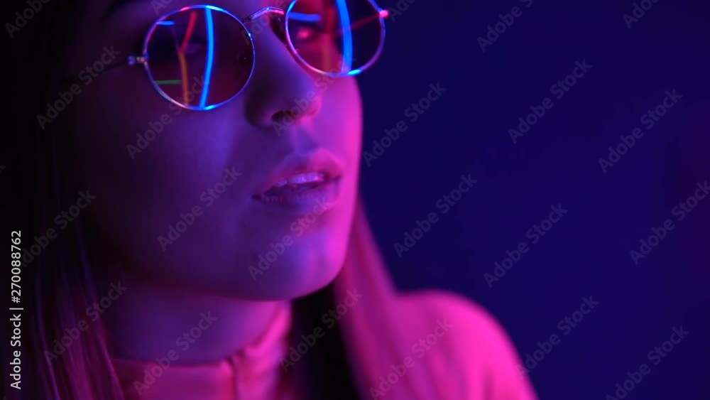 Fashionable girl in glasses on a neon background. Neon hearts are reflected in glasses. Fashionable girl in glasses on a neon background. Neon hearts are reflected in glasses.