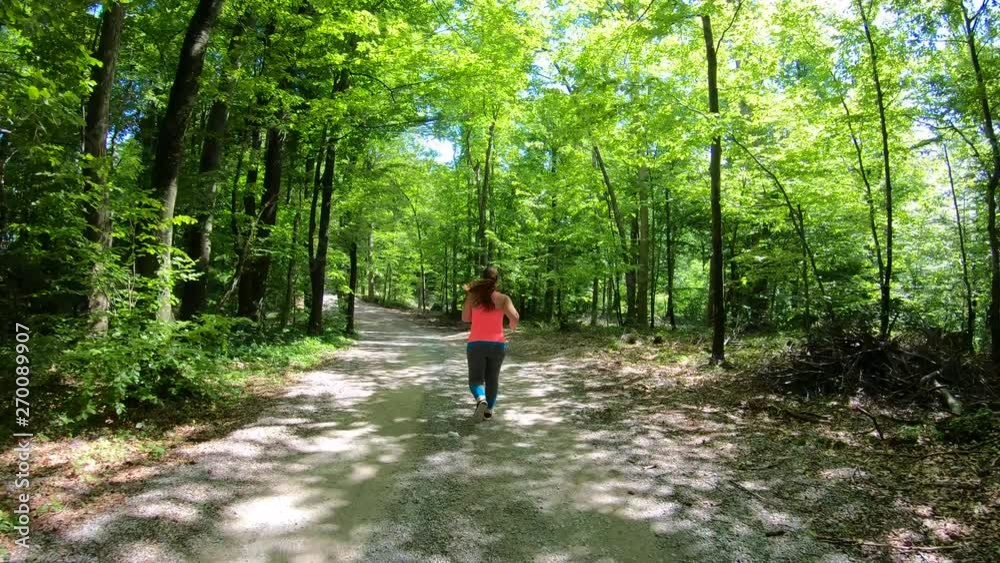 Beautiful overweight female runner leaning forward and catching her breath on the forest road 
