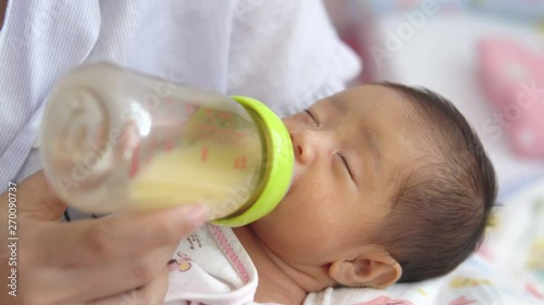 Mother holding newborn baby and feeding breast milk with milk bottle.