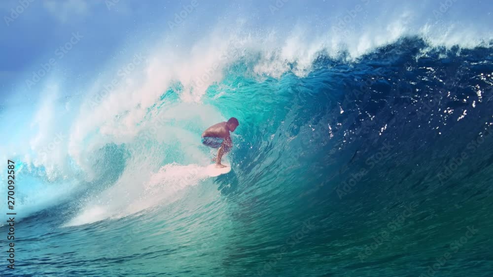 SLOW MOTION, CLOSE UP: Extreme athlete surfs a big barrel ocean wave glistening in the summer sunshine. Spectacular tube wave splashes over the surfer enjoying his active vacation in French Polynesia.
