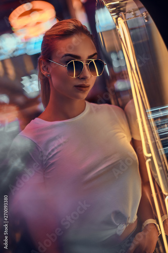 Portrait of pensive trendy woman in sunglasses and white tshirt with pink neon lights.