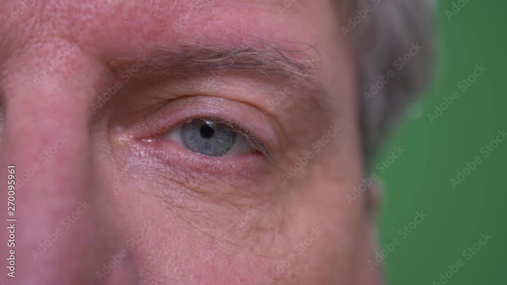 Close-up one eye portrait of depressed senior businessman watches sadly isolated on green chromakey background. Close-up one eye portrait of depressed senior businessman watches sadly isolated on green chromakey background.