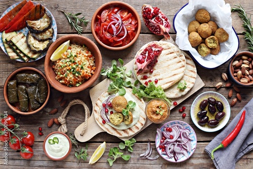 Middle eastern, arabic or mediterranean appetizers table concept with falafel, pita flatbread, bulgur and tomato salads, grilled vegetables, stuffed grape leaves,olives and nuts Fotobehang