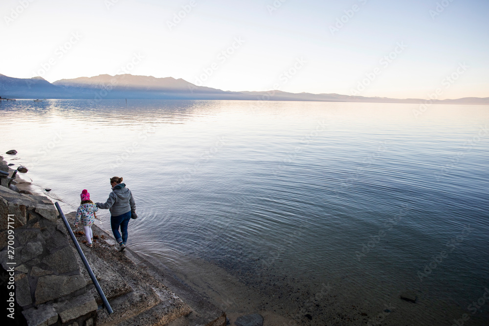A mother and daughter walking together on the shore of Lake Tahoe at sunset. A mother and daughter walking together on the shore of Lake Tahoe at sunset.