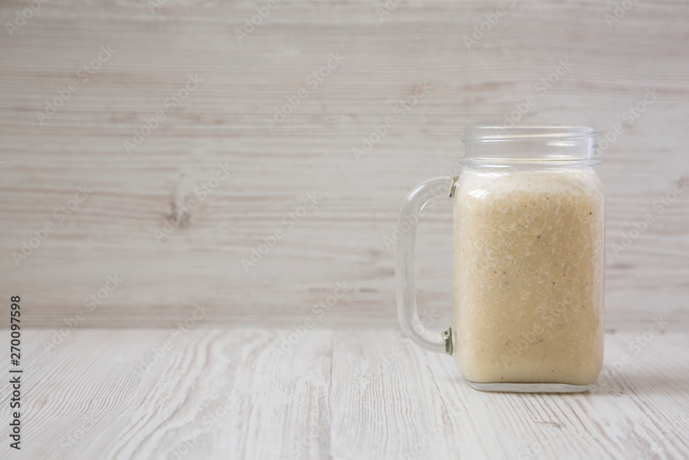Banana smoothie in a glass jar over white wooden surface, side view. Copy space. Banana smoothie in a glass jar over white wooden surface, side view. Copy space.