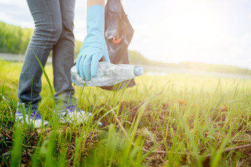 Photo of side of woman in rubber gloves picking up garbage in bag on banks of river .