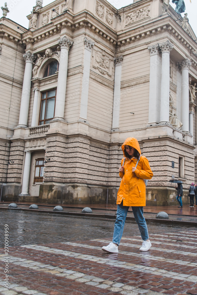 woman in orange raincoat crossing road old european building on background