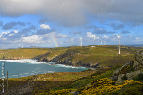 Paisaje soleado y nublado de la costa atlántica con arcoiris y molinos de viento eólicos.