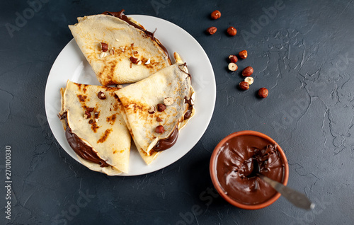 Pancakes with chocolate paste and hazelnuts, on a white plate on a background of concrete, slate