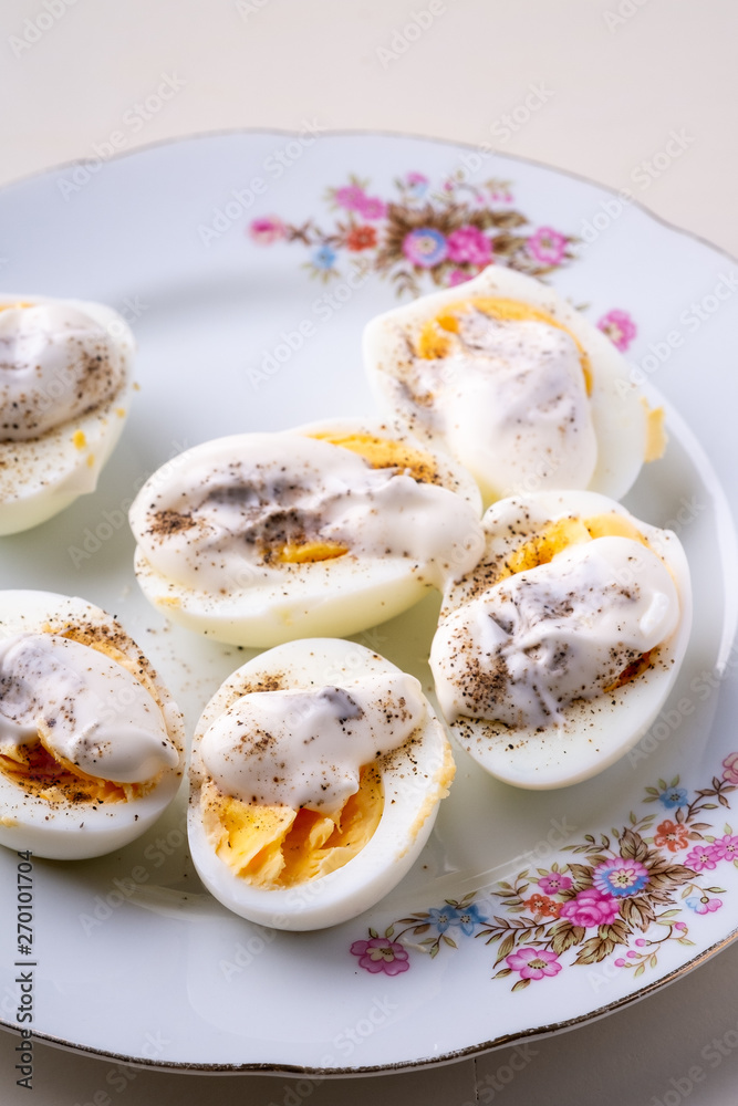 Sliced boiled eggs with mayonnaise and pepper in white plate isolated angle view Sliced boiled eggs with mayonnaise and pepper in white plate isolated angle view