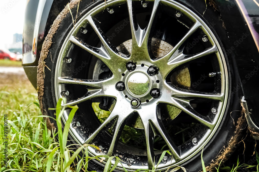 Light alloy wheel of the car is dirty with dirt. The car is on the field.