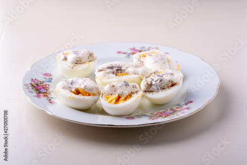 Sliced boiled eggs with mayonnaise and pepper in white plate isolated angle view