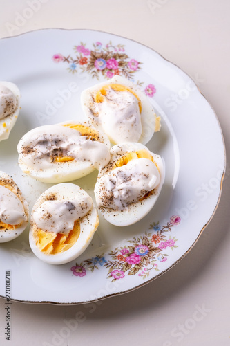 Sliced boiled eggs with mayonnaise and pepper in white plate isolated angle view