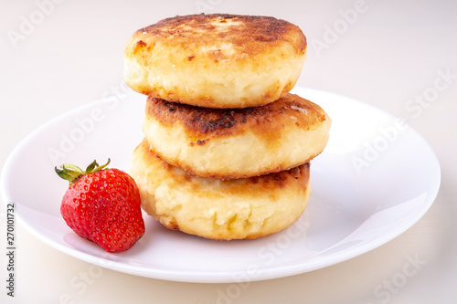 Cottage cheese pancakes with one strawberry on white plate isolated angle view