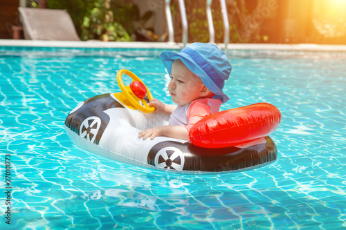 Kid behind the wheel in the pool. Summer vacation at sea. A little girl less than one year old is driving an inflatable boat in the shape of a car.