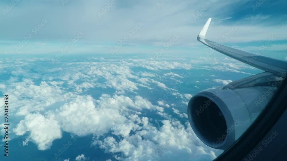 View through the window of an airplane of the wing and turbine. Airplane flying high, clouds moving below the plane.