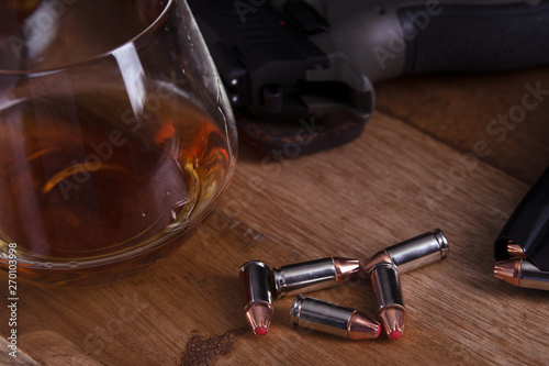 gun and glass of cognac on wooden table
