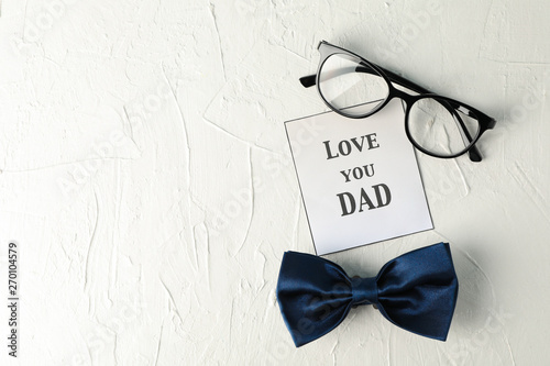 Inscription love you DAD, blue bow tie and glasses on white background, space for text and top view