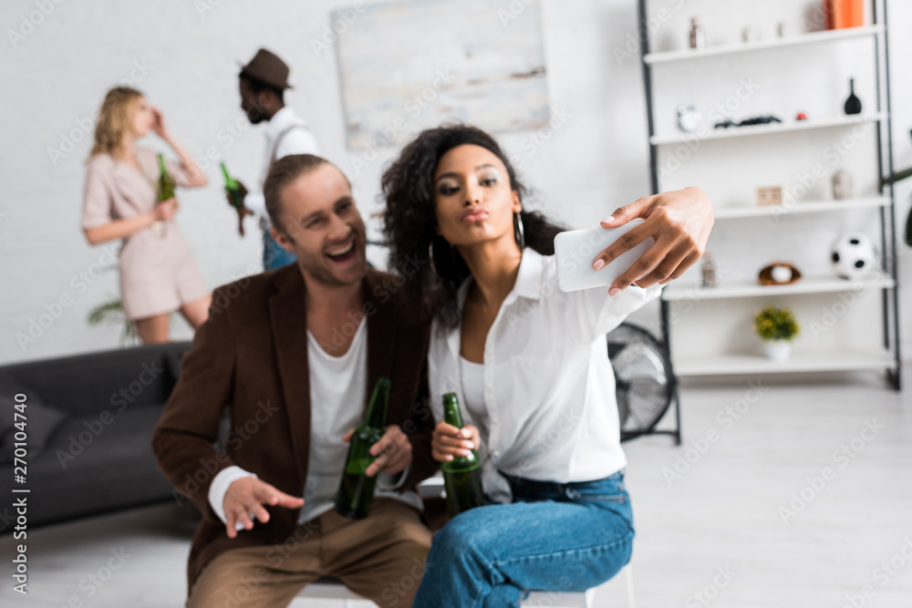 selective focus of african american girl with duck face taking selfie with cheerful man