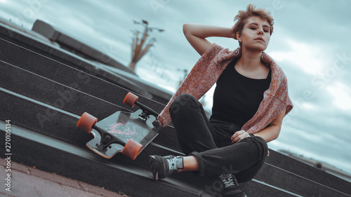 A beautiful young girl holding a skateboard while sitting in skatepark at the city