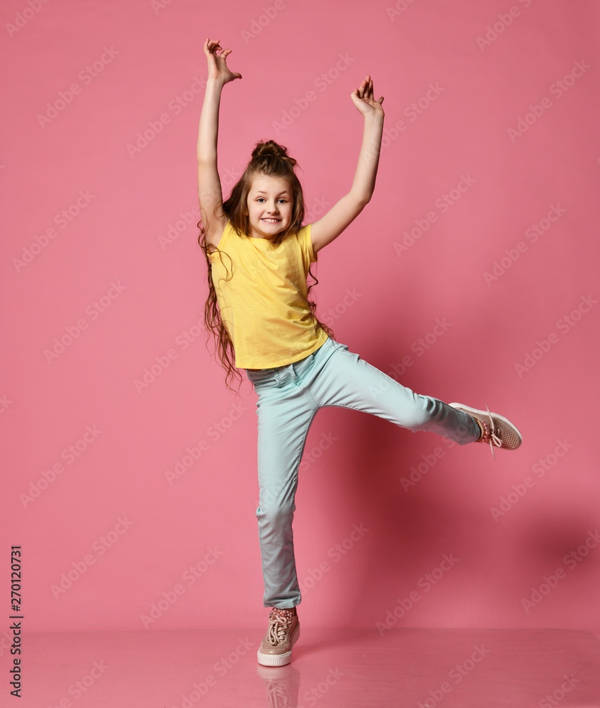 Young lady or teen girl in jeans and yellow t-shirt has fun taking funny  poses with her hands and leg up Stock Photo