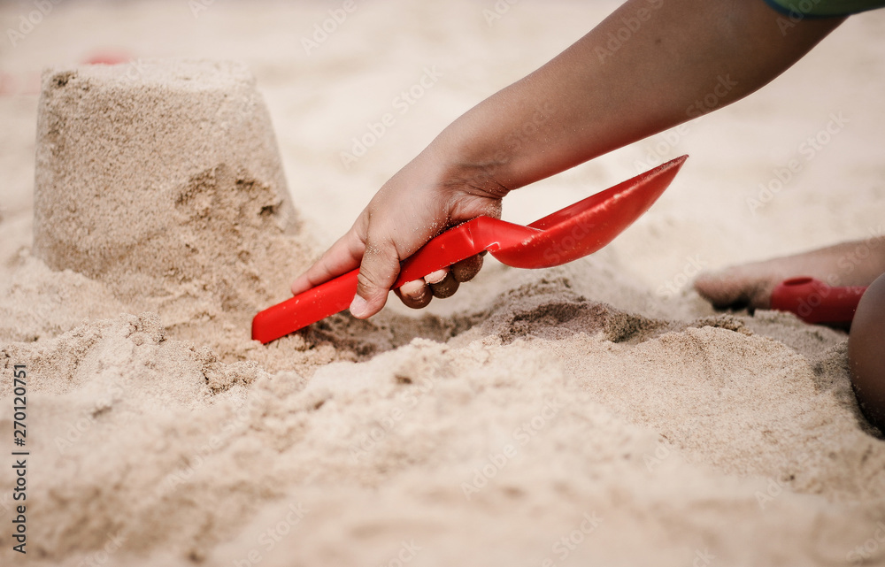 Kind spielt mit roter Schaufel am Strand und baut eine Sandburg Kind spielt mit roter Schaufel am Strand und baut eine Sandburg
