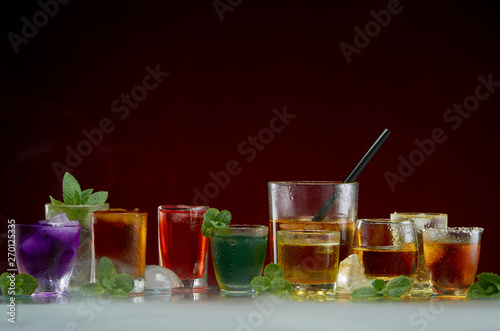 Color septet of alcoholic beverages in transparent glass glasses with ice and mint in smoke on a red background