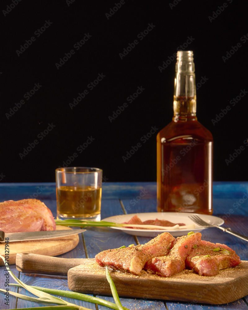 Fresh meat with spices on wooden Board and alcohol standing on blue table and black background