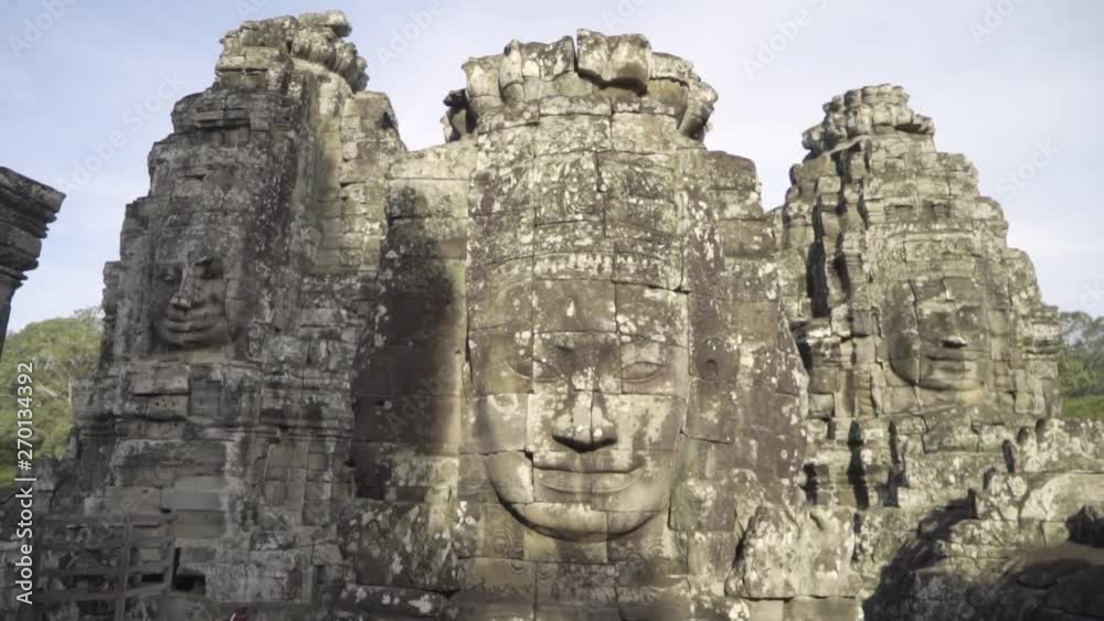 Walking away from a stone face at Bayon temple in Cambodia to reveal more stone faces in the background. Walking away from a stone face at Bayon temple in Cambodia to reveal more stone faces in the background.