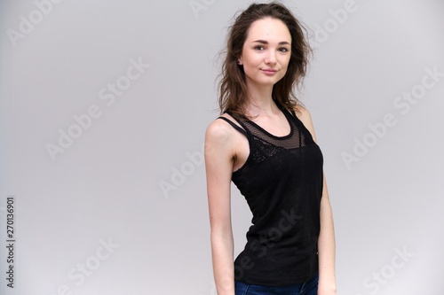 Life is a success. I am pleased with myself. Concept photo of a happy smiling woman satisfied life contented brunette girl in a black T-shirt and jeans on a gray background with flowing hair.