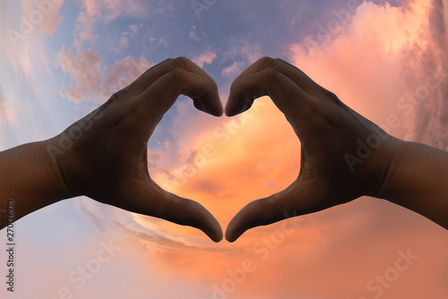 Man's hands make a heart shape. With a sky background