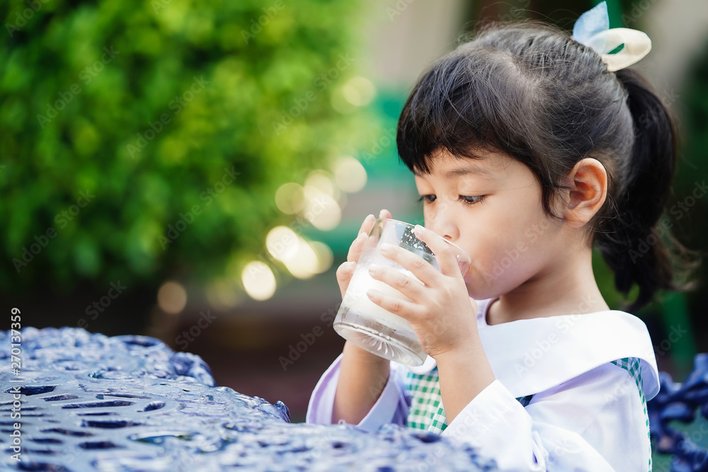 Asian cute student girl drinking a glass of milk at home before going to school in the morning. The concept is healthy and intelligent kid concept. Asian cute student girl drinking a glass of milk at home before going to school in the morning. The concept is healthy and intelligent kid concept.