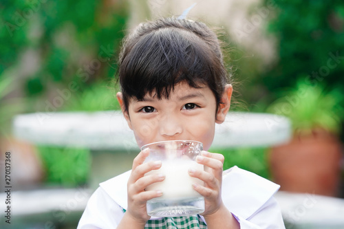 Asian cute student girl drinking a glass of milk at home before going to school in the morning. The concept is healthy and intelligent kid concept.    