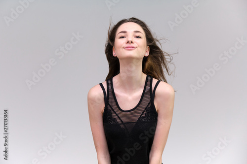 Life is a success. I am pleased with myself. Concept photo of a happy smiling woman satisfied life contented brunette girl in a black T-shirt and jeans on a gray background with flowing hair.