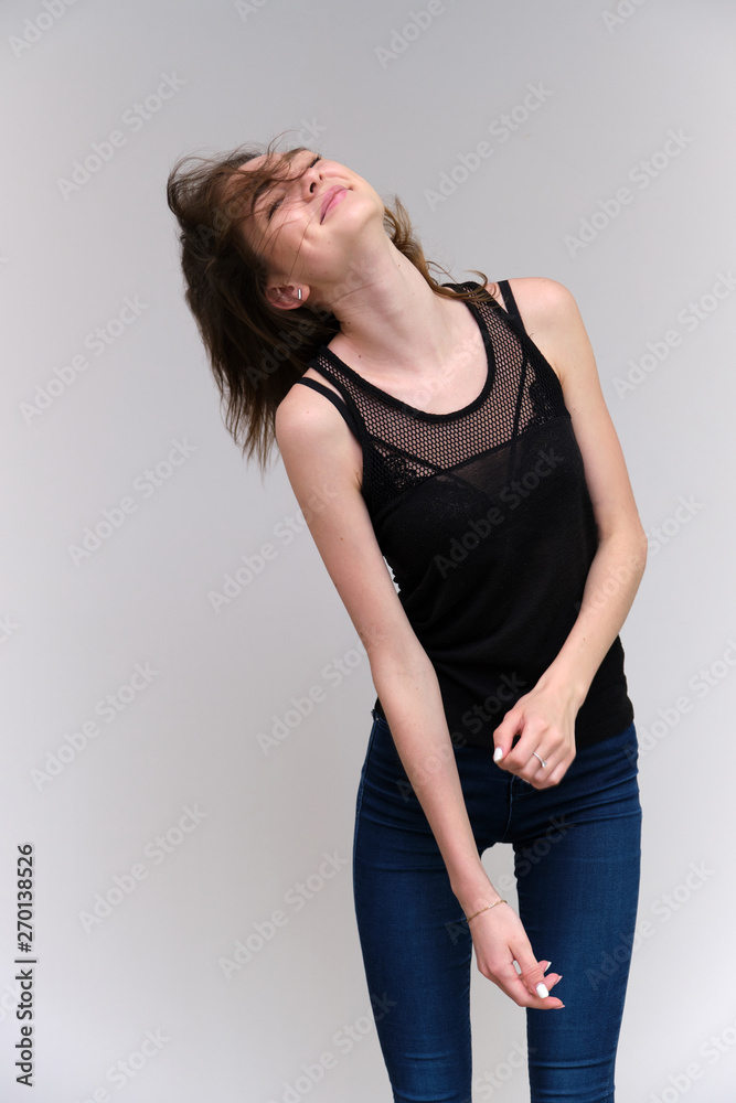 Life is a success. I am pleased with myself. Concept photo of a happy smiling woman satisfied life contented brunette girl in a black T-shirt and jeans on a gray background with flowing hair. Life is a success. I am pleased with myself. Concept photo of a happy smiling woman satisfied life contented brunette girl in a black T-shirt and jeans on a gray background with flowing hair.