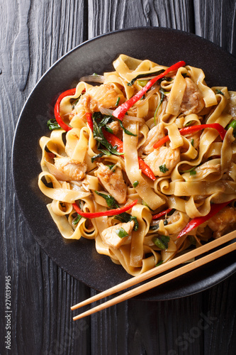 Drunken noodles pad kee mao with chicken, basil, chili pepper and sauce close-up on a plate. Vertical top view