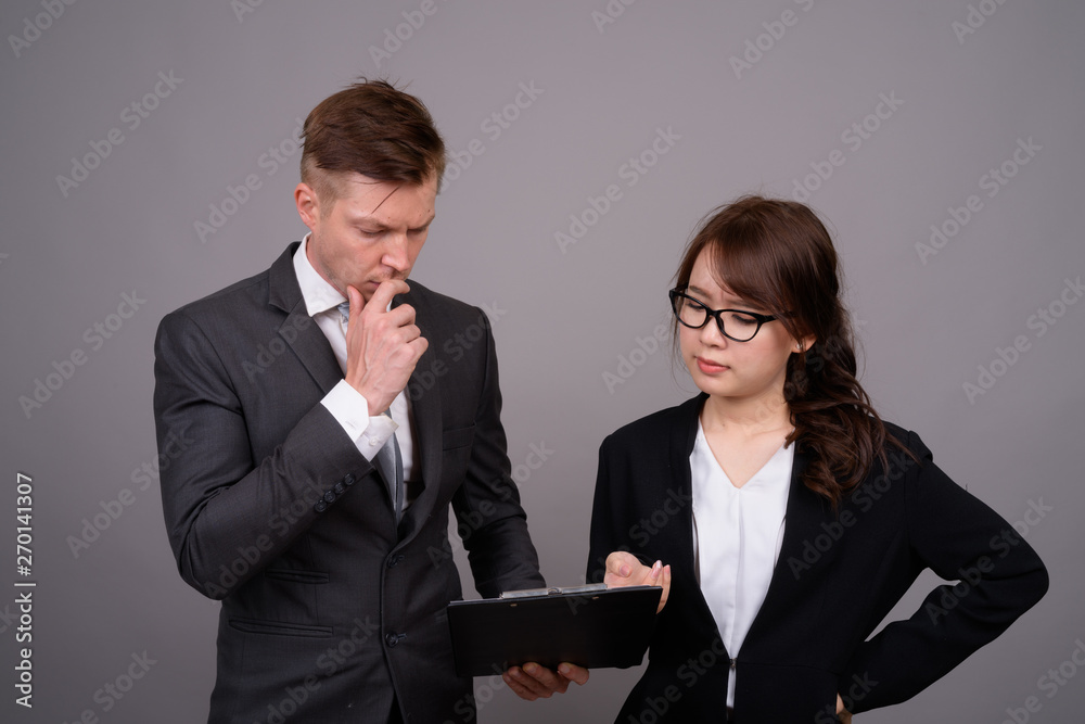 Young businessman and young Asian businesswoman against gray bac