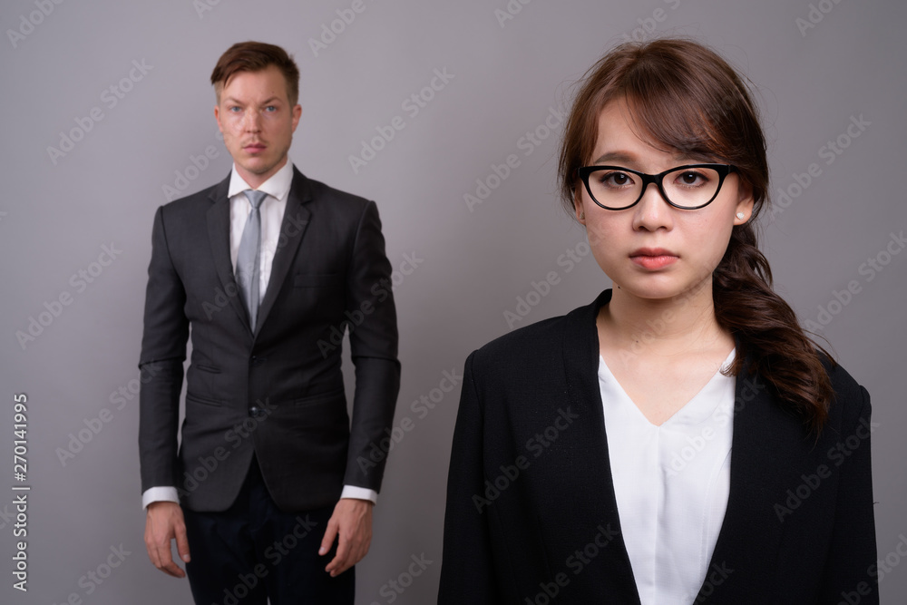 Young businessman and young Asian businesswoman against gray bac