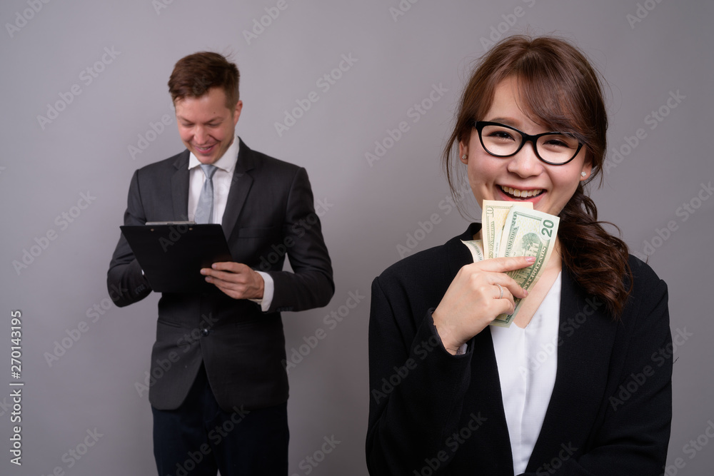Young businessman and young Asian businesswoman against gray bac Young businessman and young Asian businesswoman against gray bac