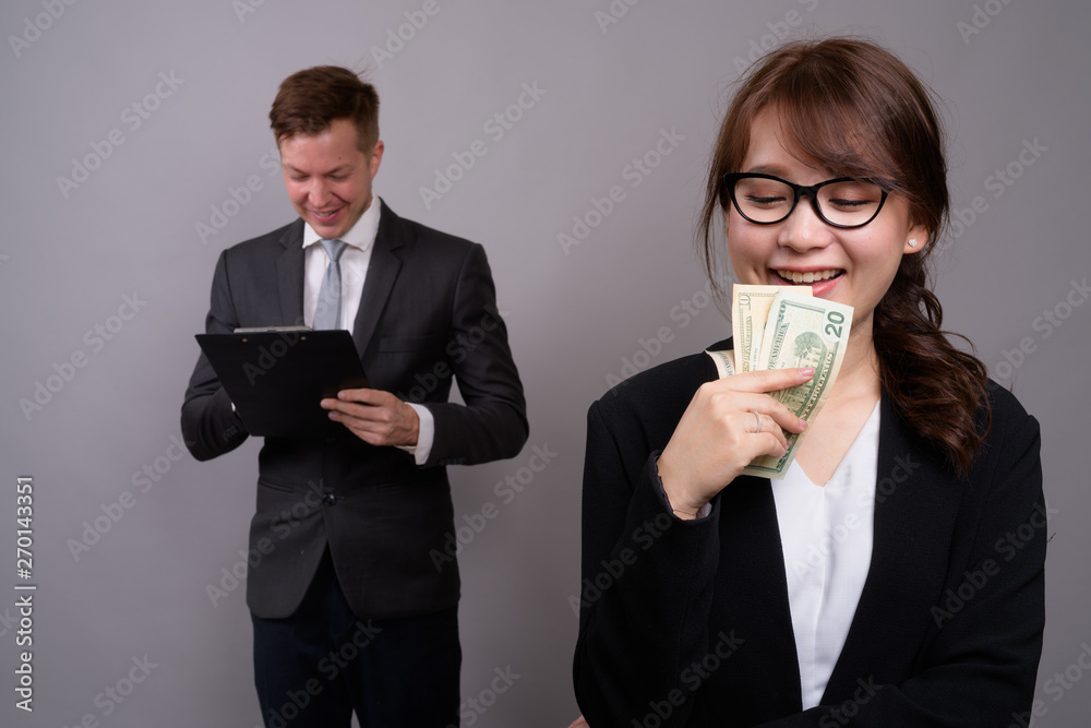 Young businessman and young Asian businesswoman against gray bac Young businessman and young Asian businesswoman against gray bac
